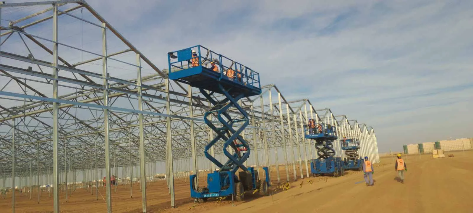 Crews on scissor lifts assembling greenhouse steel structures